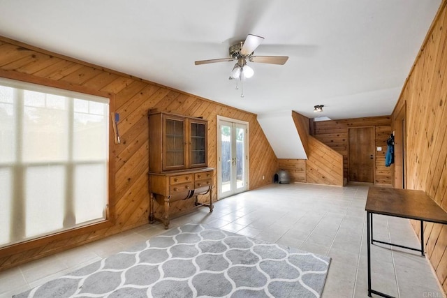 bonus room featuring french doors, a ceiling fan, light tile patterned flooring, and wooden walls