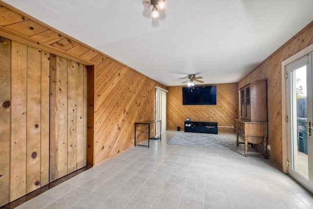 unfurnished living room with a ceiling fan and wood walls