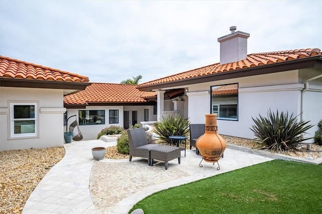 rear view of house with a patio area, stucco siding, a tile roof, and a chimney