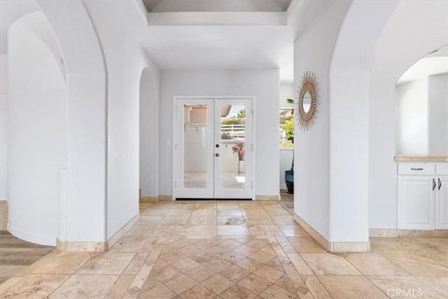 entryway with stone tile floors, arched walkways, baseboards, and french doors