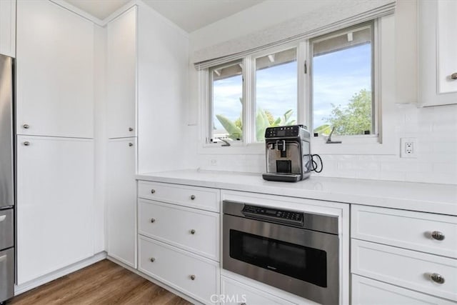 kitchen featuring decorative backsplash, wood finished floors, a healthy amount of sunlight, light countertops, and white cabinetry