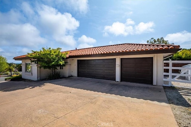 view of front facade with a tile roof, fence, concrete driveway, an attached garage, and stucco siding