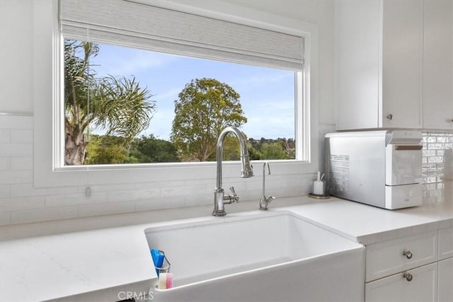 kitchen featuring light countertops, white cabinets, a sink, and tasteful backsplash