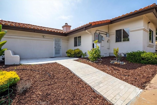 mediterranean / spanish-style home featuring a patio, a chimney, stucco siding, and a tile roof
