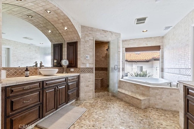full bathroom featuring vanity, a garden tub, tile walls, and visible vents