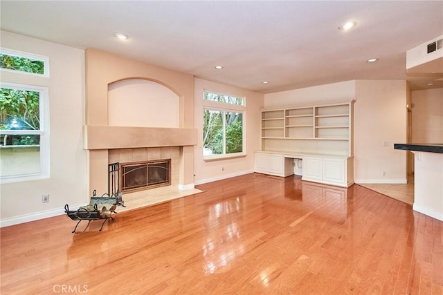 unfurnished living room featuring a tiled fireplace, baseboards, recessed lighting, and wood finished floors