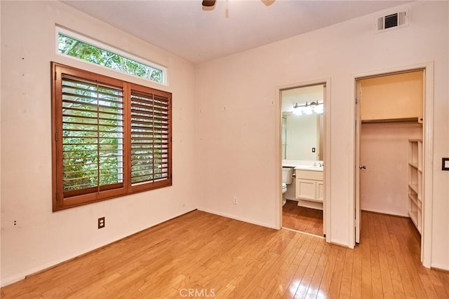 unfurnished bedroom with connected bathroom, a walk in closet, light wood-type flooring, visible vents, and a closet