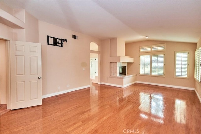 unfurnished living room with a fireplace, light wood-style floors, baseboards, lofted ceiling, and visible vents
