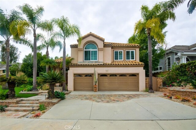 mediterranean / spanish-style house featuring a tiled roof, a garage, stucco siding, and driveway