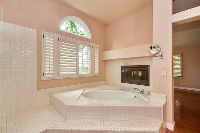 bathroom featuring baseboards, a tile fireplace, a bath, and wood finished floors