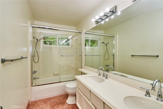full bathroom with double vanity, a sink, combined bath / shower with glass door, and toilet