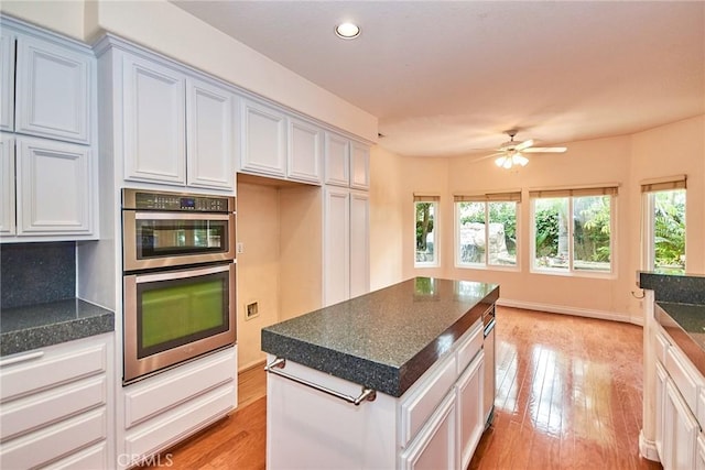 kitchen with dark countertops, stainless steel double oven, light wood-style flooring, a ceiling fan, and recessed lighting