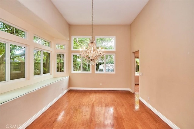 unfurnished dining area with light wood-style floors, baseboards, a high ceiling, and a wealth of natural light