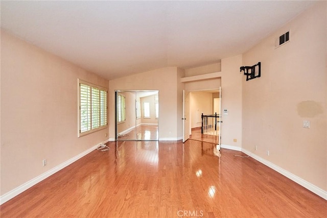 empty room with baseboards, visible vents, vaulted ceiling, and light wood finished floors