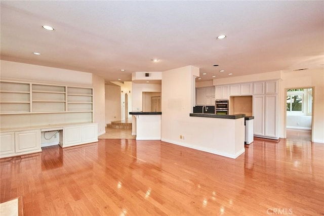 unfurnished living room featuring light wood-style floors, baseboards, recessed lighting, and built in desk