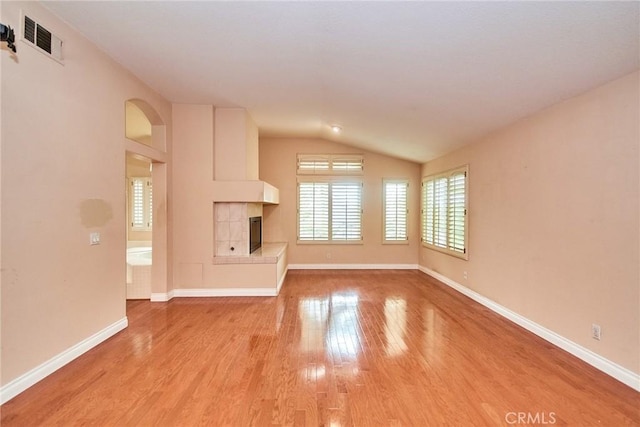 unfurnished living room with visible vents, lofted ceiling, a fireplace, baseboards, and light wood-style floors