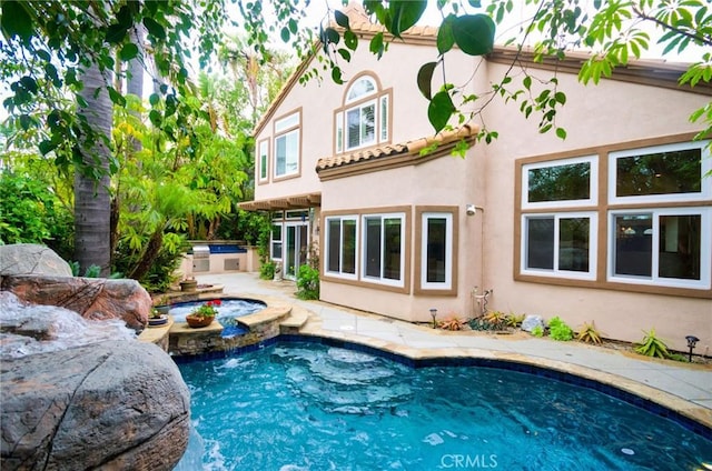 back of house featuring an outdoor kitchen, an outdoor pool, and stucco siding