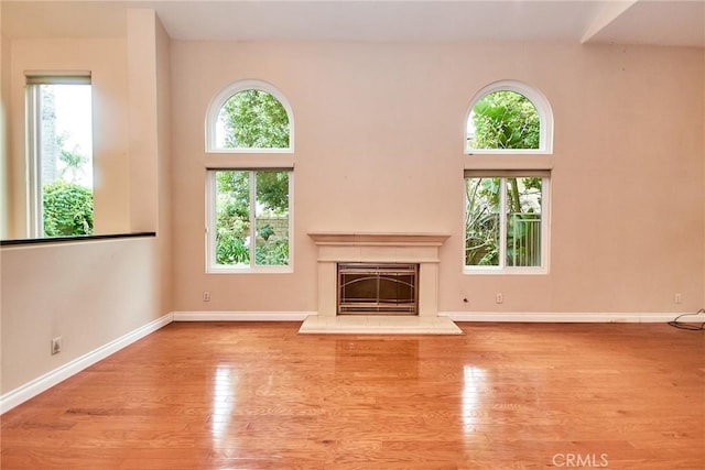 unfurnished living room with a fireplace with raised hearth, baseboards, and wood finished floors