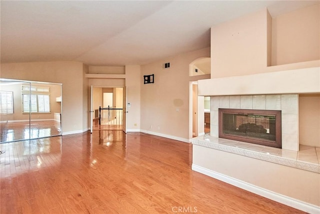 unfurnished living room featuring visible vents, wood finished floors, baseboards, a tiled fireplace, and vaulted ceiling
