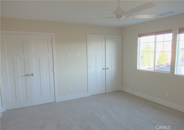 unfurnished bedroom featuring baseboards, visible vents, two closets, and light colored carpet