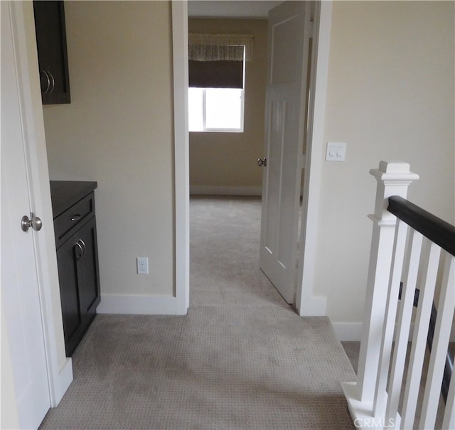 hall with baseboards, an upstairs landing, and light carpet