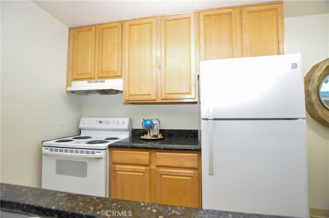 kitchen featuring light brown cabinetry, dark stone counters, under cabinet range hood, and white appliances
