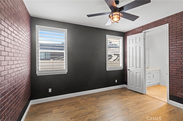 unfurnished bedroom featuring brick wall, multiple windows, baseboards, and hardwood / wood-style floors