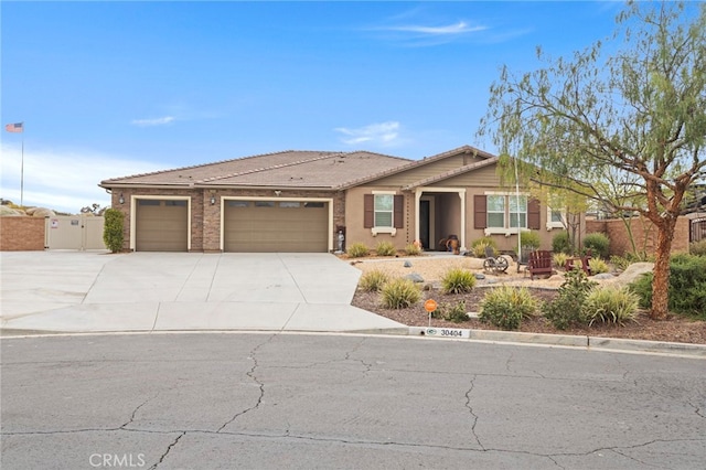 ranch-style home with a tiled roof, a gate, a garage, concrete driveway, and stucco siding