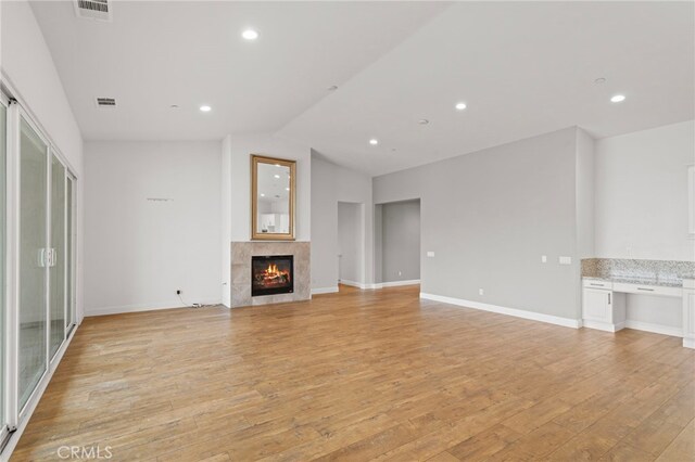 unfurnished living room featuring visible vents, a high end fireplace, lofted ceiling, and light wood-type flooring