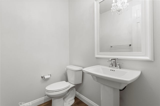 bathroom with a notable chandelier, a sink, toilet, baseboards, and wood finished floors