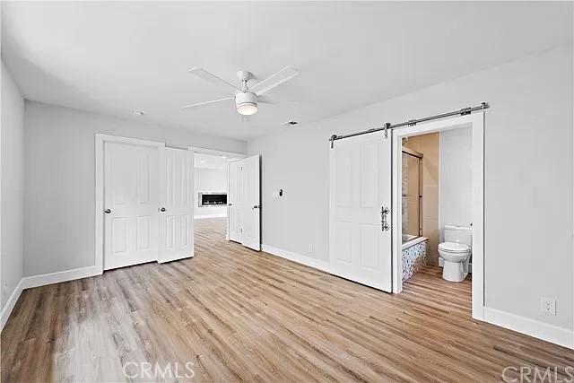 26872 Vista Del Mar, Dana Point, CA 92624 - unfurnished bedroom with ceiling fan, a barn door, baseboards, ensuite bathroom, and light wood-style flooring