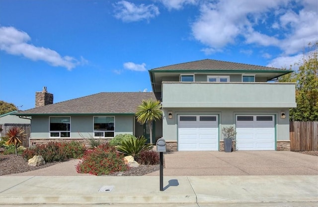 view of front of home featuring fence, stucco siding, a chimney, concrete driveway, and a balcony