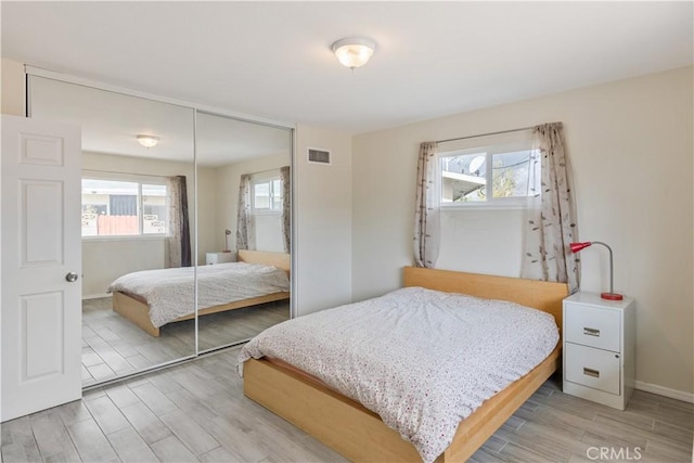 bedroom featuring visible vents, light wood finished floors, baseboards, and a closet