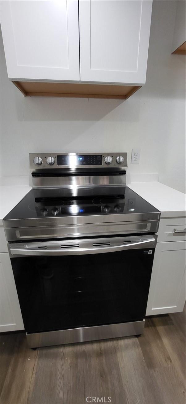 interior details featuring light countertops, dark wood-style flooring, stainless steel electric stove, and white cabinets