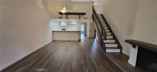 interior space with a high ceiling, ceiling fan, baseboards, dark wood-style floors, and stairway