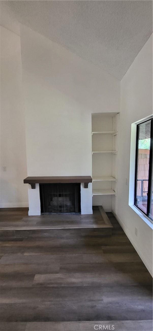 unfurnished living room featuring a textured ceiling, a fireplace, dark wood finished floors, baseboards, and lofted ceiling