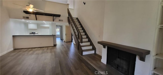 unfurnished living room featuring a towering ceiling, a ceiling fan, baseboards, dark wood-type flooring, and stairway