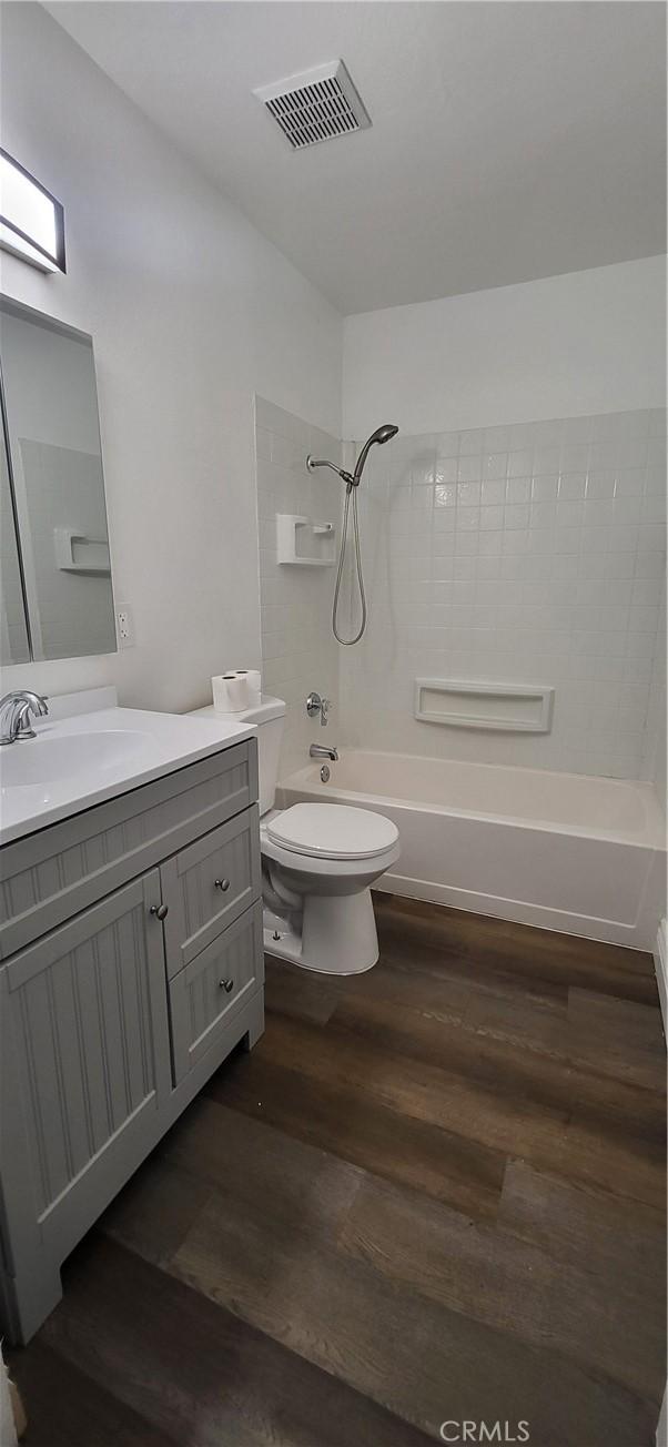bathroom featuring visible vents, wood finished floors, vanity, toilet, and  shower combination