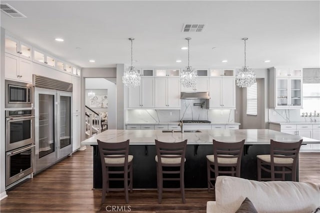 kitchen featuring built in appliances, backsplash, dark wood-style flooring, and a notable chandelier