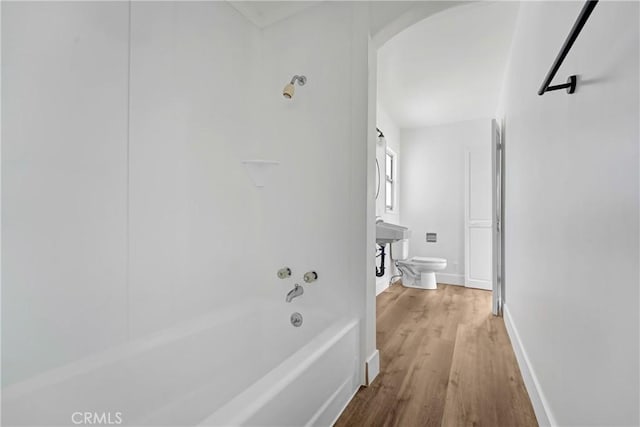 corridor with arched walkways, baseboards, and wood finished floors