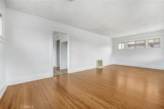 empty room with baseboards, a textured ceiling, and wood finished floors