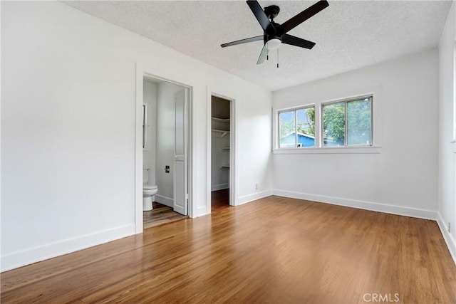 unfurnished bedroom with a textured ceiling, baseboards, wood finished floors, and a walk in closet