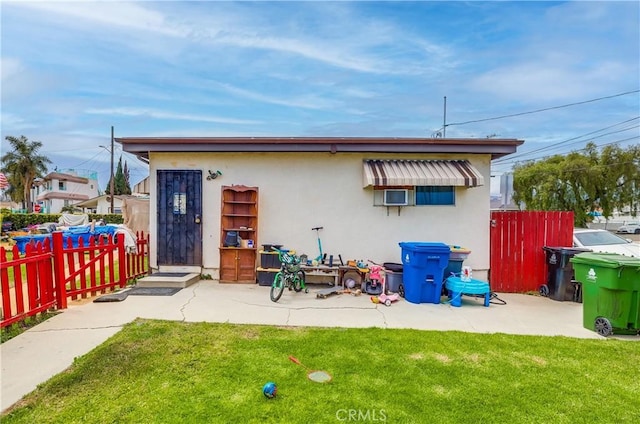 rear view of house featuring a lawn, fence, and stucco siding
