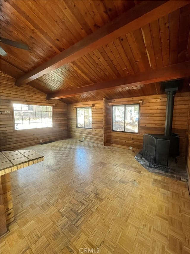 unfurnished living room with wood ceiling, lofted ceiling with beams, a wood stove, and wood walls