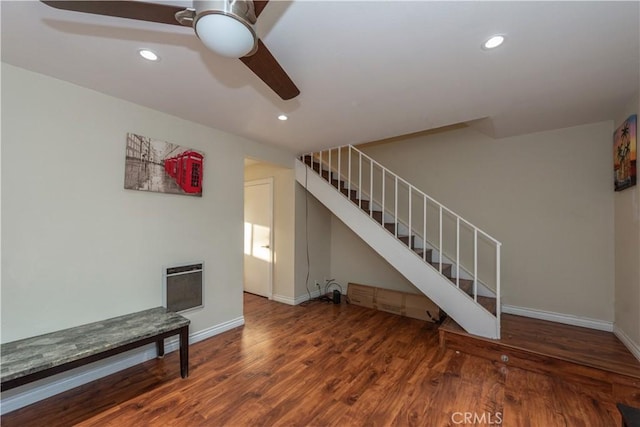 unfurnished living room with a ceiling fan, baseboards, heating unit, stairway, and wood finished floors