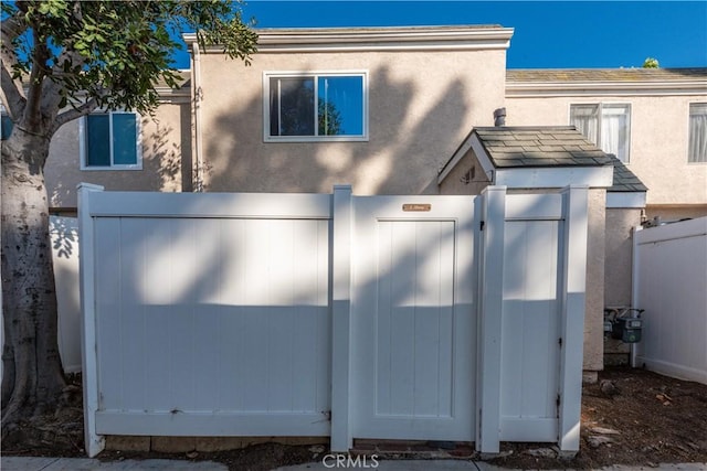 view of side of home with fence, stucco siding, and a gate