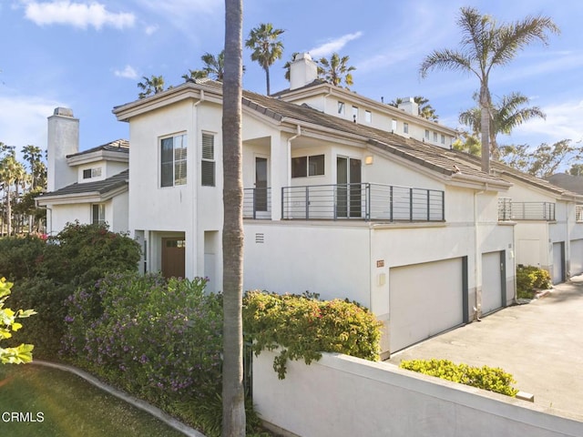 view of front of home with a chimney, concrete driveway, stucco siding, and a balcony