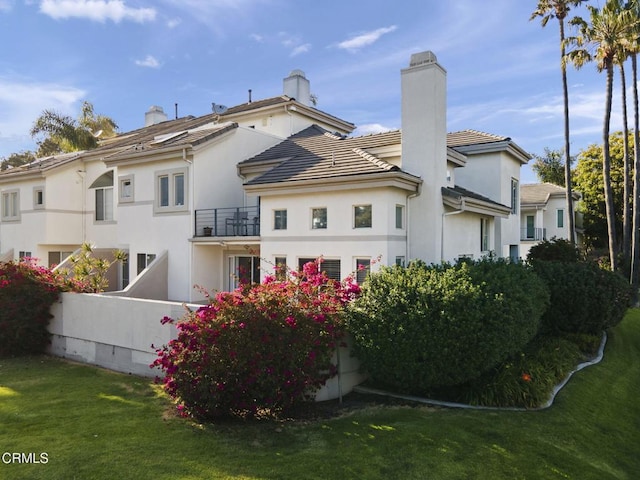back of property featuring a tiled roof, a chimney, a yard, and stucco siding