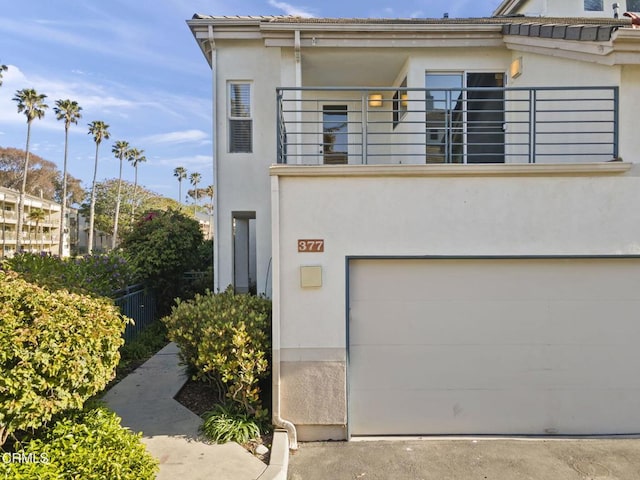 view of front facade featuring a garage, fence, a balcony, and stucco siding