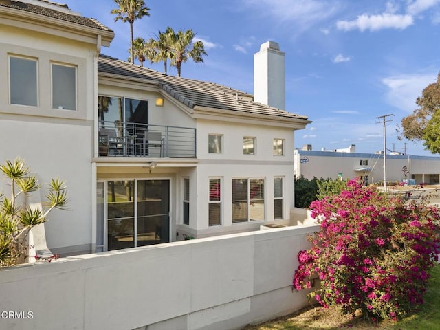 rear view of property featuring fence, a tile roof, stucco siding, a chimney, and a balcony